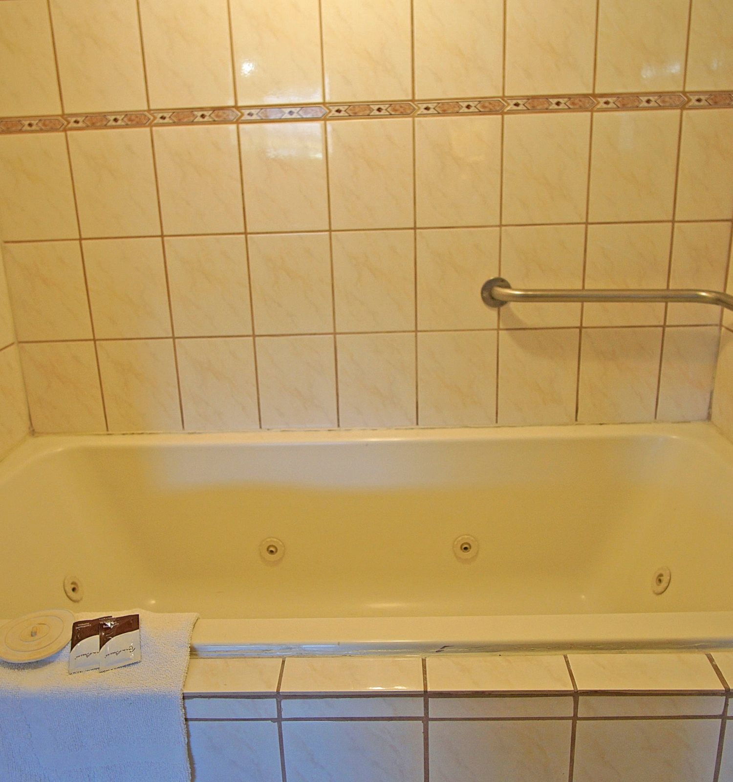 The image shows a tiled bathtub with a towel hanging over the edge, a grab bar on the wall, and a faucet with a shower attachment.