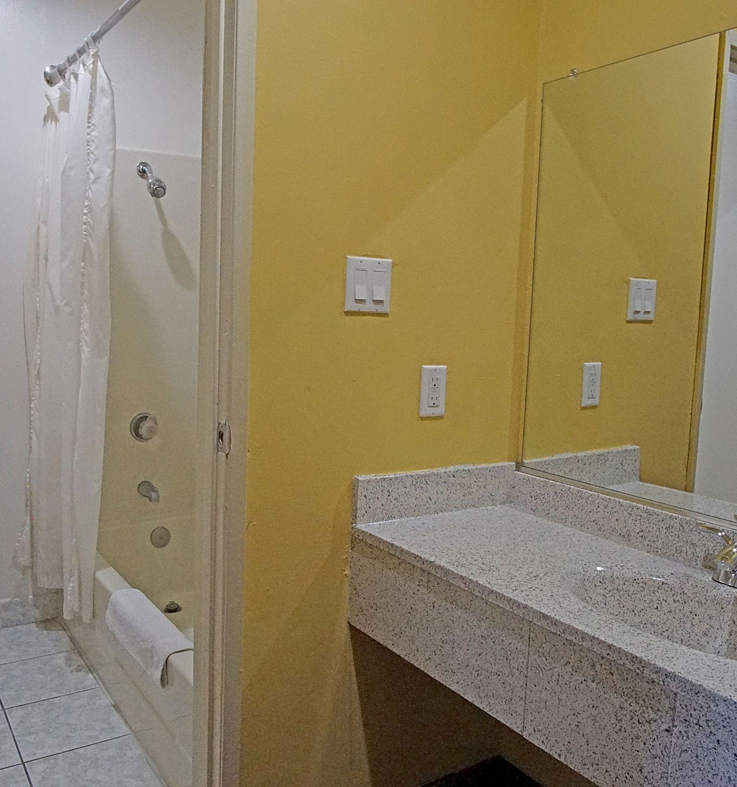 A bathroom with a toilet, a bathtub with a shower curtain, a sink with a countertop, and a large mirror on the wall.