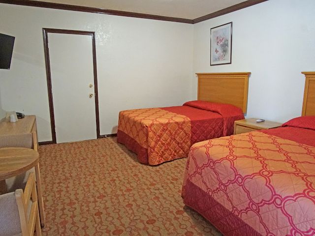 A wide view of a hotel room with two beds, a desk, and a TV.