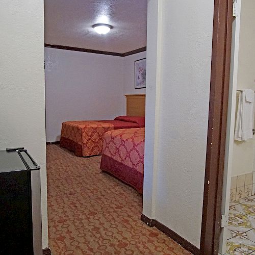 This image shows a hotel room with two beds, a small refrigerator, and a view into the bathroom with a tub and shower combination.