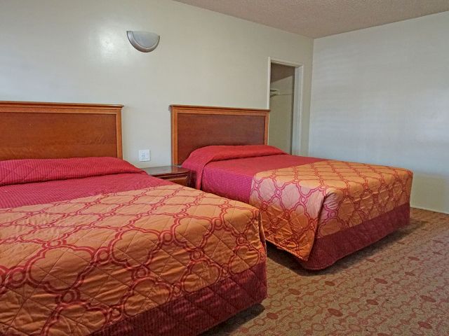 A hotel room with two beds, wooden headboards, and red and orange bedding.