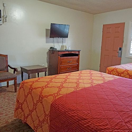 A hotel room with two beds, a TV, an air conditioner, a small fridge, a microwave, a chair, a table, and a pink door.