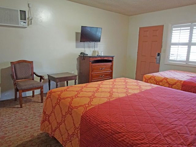 A hotel room with two beds, a TV on the wall, a dresser, a chair, and a window.