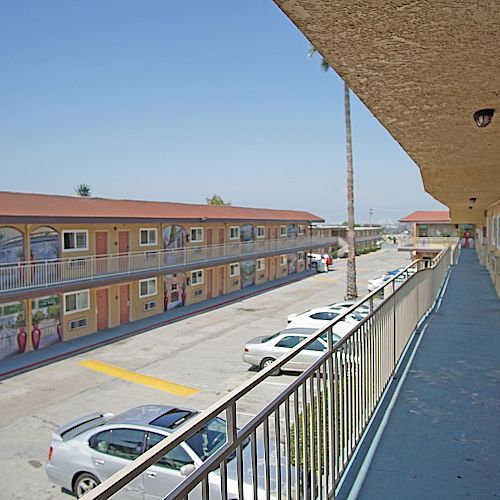 The image shows an outdoor view of a two-story motel with parked cars and a walkway along the upper floor. The sky is clear and blue.