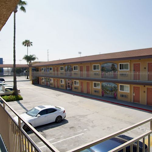 This image depicts a two-story motel with parked cars in an open courtyard. The motel has exterior corridors and palm trees nearby.