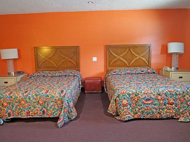 A hotel room with two beds, two nightstands, and two lamps.