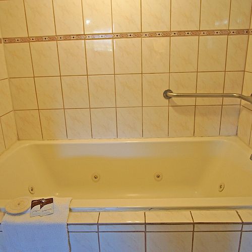 The image shows a tiled bathtub with a grab bar on the right wall and a folded towel placed on the edge of the bathtub.