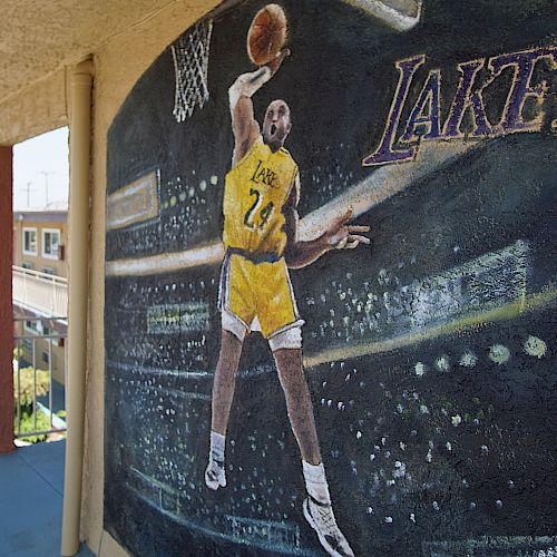 A mural of a basketball player in a yellow Lakers jersey, number 24, jumping to make a shot with the word 