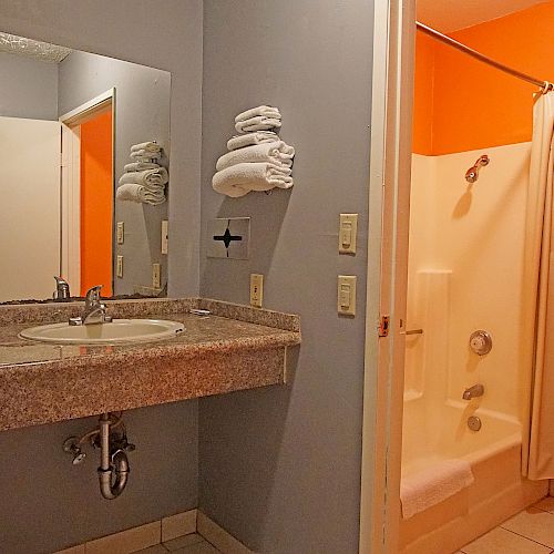 This image shows a bathroom with a sink and mirror, towels, a shower with a curtain, and a toilet. The walls are orange and gray.