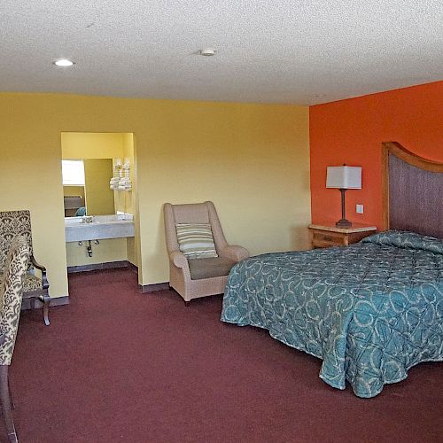 This image shows a hotel room with a bed, two lamps, a TV, a desk, chairs, and an open doorway leading to a bathroom.