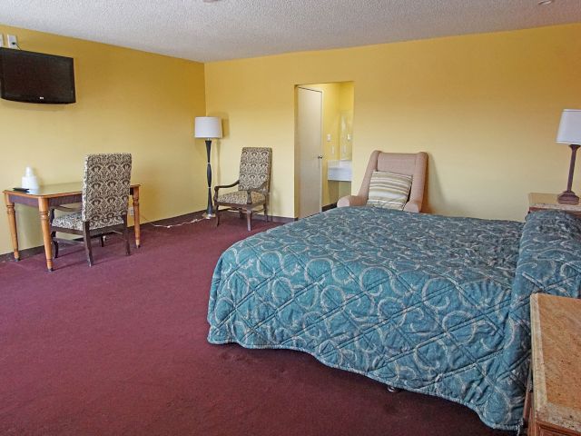 A wide view of a hotel room with a bed, desk, chairs, and TV.