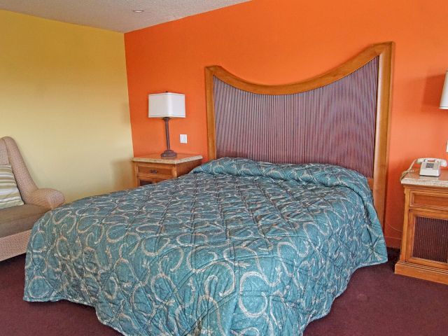 A wide view of a hotel room with a bed, nightstands, a chair, and a telephone.