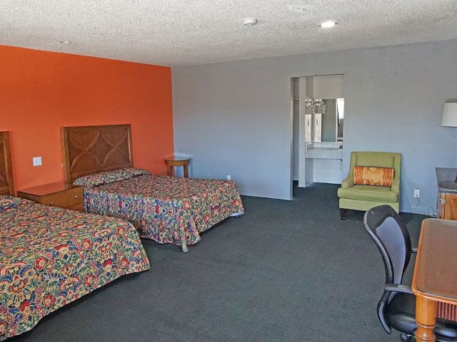 A wide view of a hotel room with two beds, a desk, and a chair.