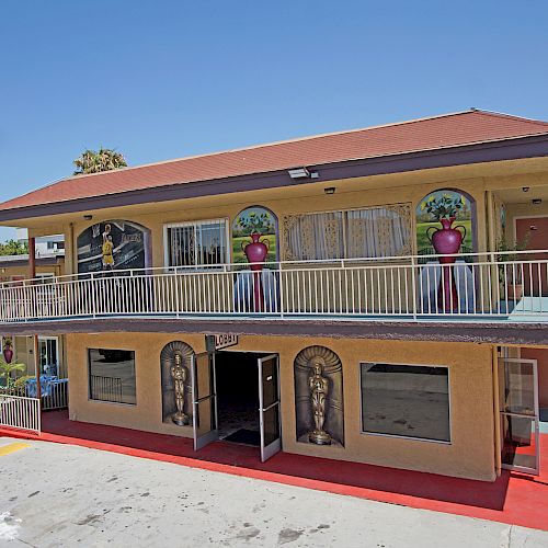 This image shows a two-story motel with decorative columns and arched entryways, parking spaces in front, and a mural on the upper tier of the building.