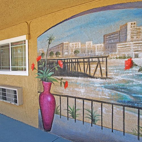 The image shows a mural depicting a coastal city view with buildings, a pier, and ocean waves, with red flower vases in the foreground, next to a door.