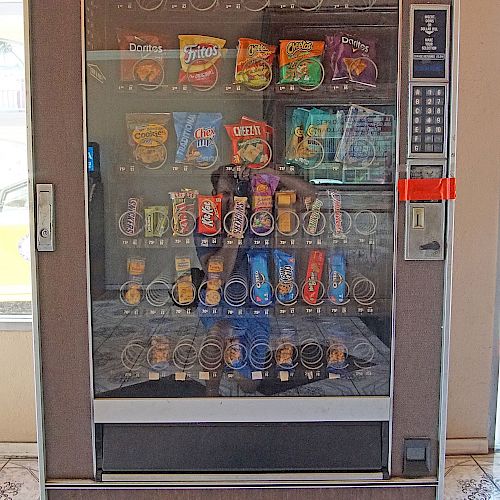 A vending machine filled with various snacks, including chips and candies, is shown. The selection consists of multiple rows and columns of treats.