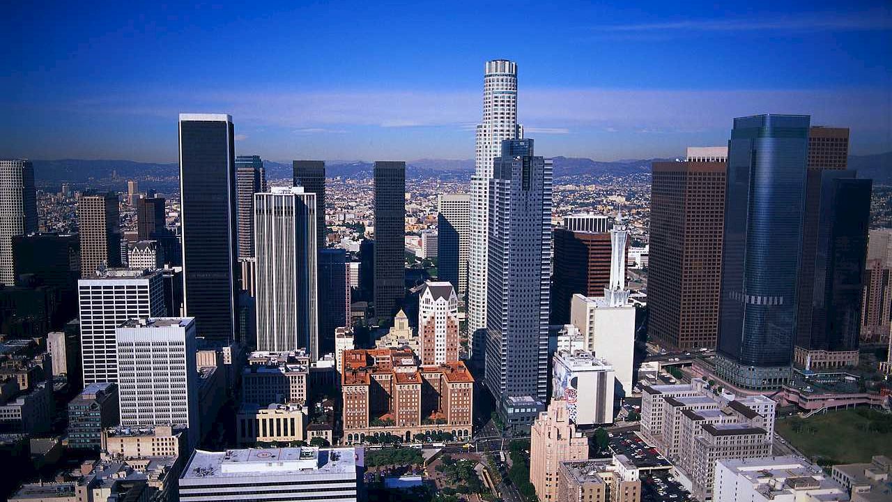 An image of a modern city skyline with numerous high-rise buildings, under a clear blue sky, showcasing an urban downtown area with diverse architecture.