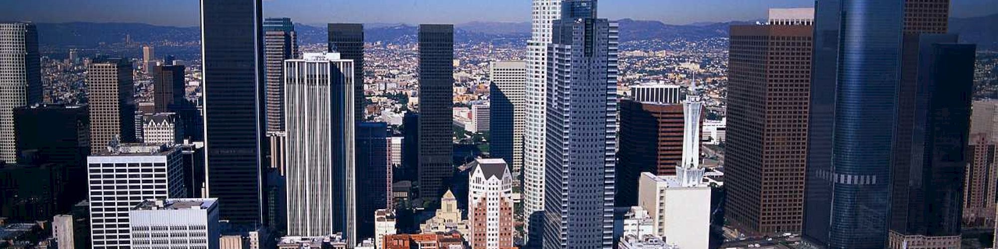 An image of a modern city skyline with numerous high-rise buildings, under a clear blue sky, showcasing an urban downtown area with diverse architecture.