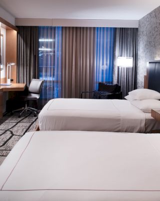 The image shows a modern hotel room with two beds, a wall-mounted TV, a desk with a chair, and contemporary decor, ending the sentence.