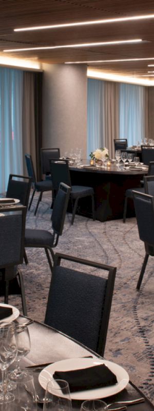 The image shows a banquet hall set up with round tables, chairs, table settings, and centerpieces, ready for a formal event or dinner.