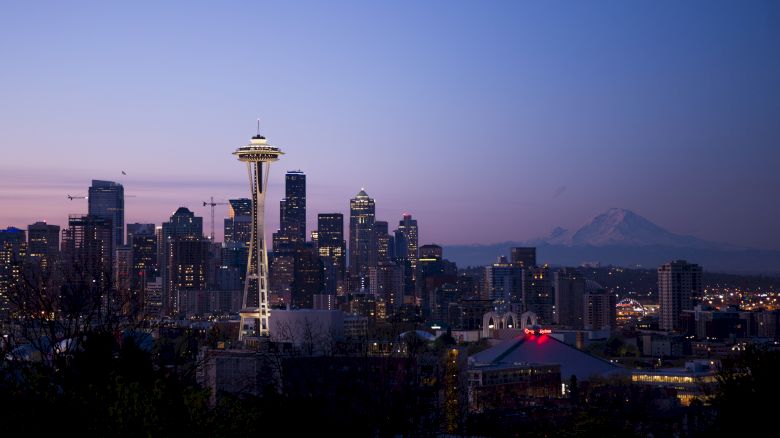 The image shows the Seattle skyline at dusk, with the Space Needle prominently featured and Mount Rainier visible in the background.