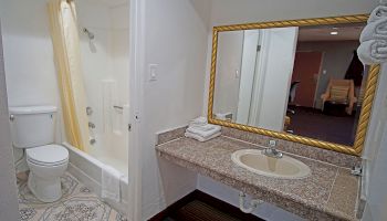 The image shows a bathroom with a toilet, a shower/tub with a yellow curtain, and a sink with a large mirror and neatly folded towels.