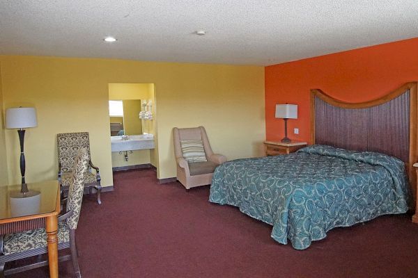 A wide view of a hotel room with a bed, chair, lamp, and doorway to the bathroom.