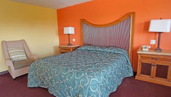 A hotel room with a double bed, green comforter, two bedside tables with lamps, an armchair, and an orange and yellow wall.