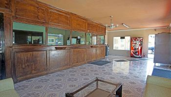 The image shows a reception area with a wooden counter, tiled floor, a soda vending machine, chairs, and a small table.