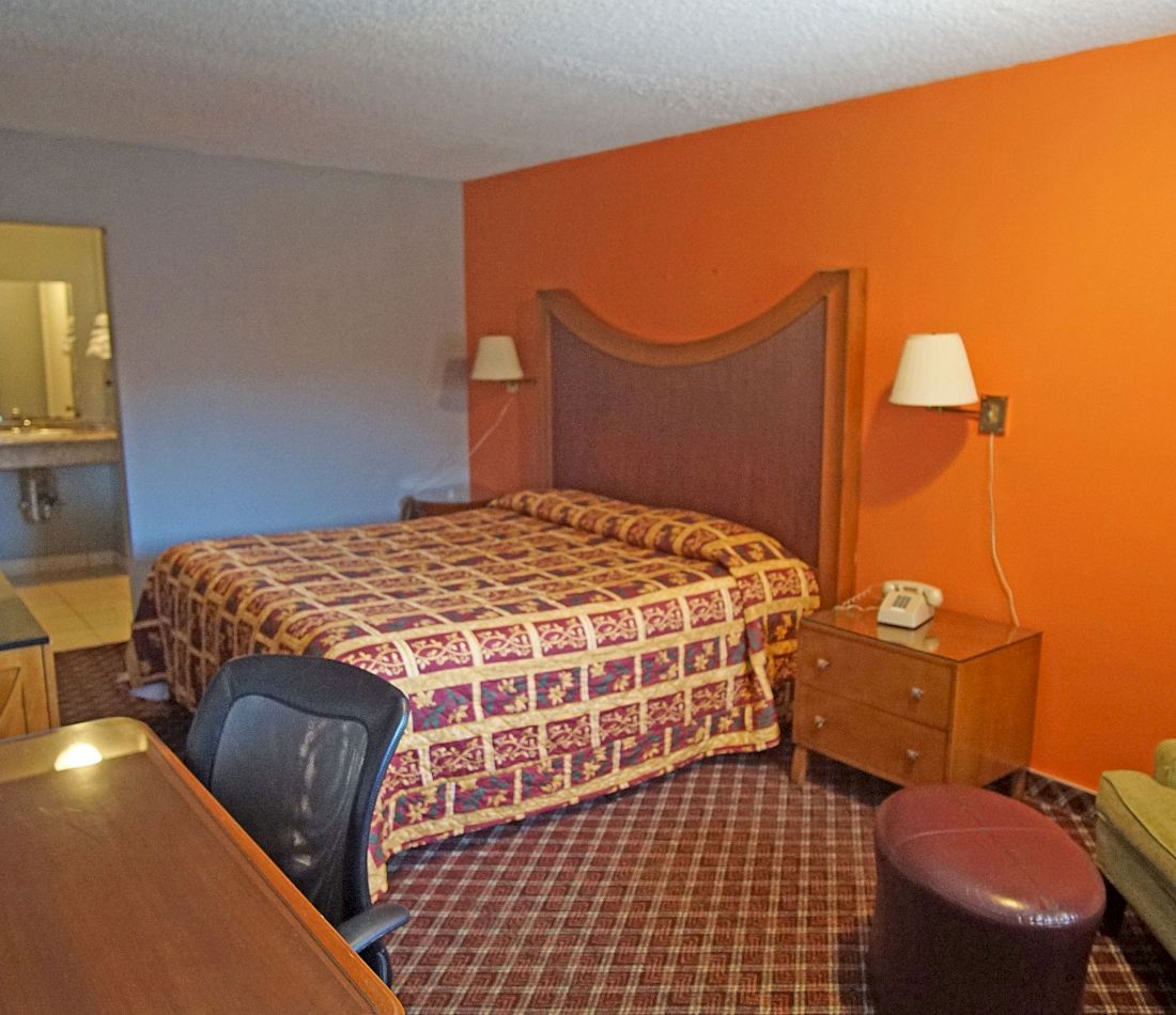 A hotel room with a bed, nightstand, desk, chair, and stool.