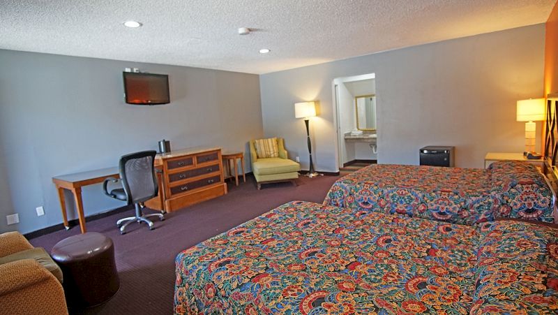 A hotel room with two beds, a desk, chair, TV, and dresser.